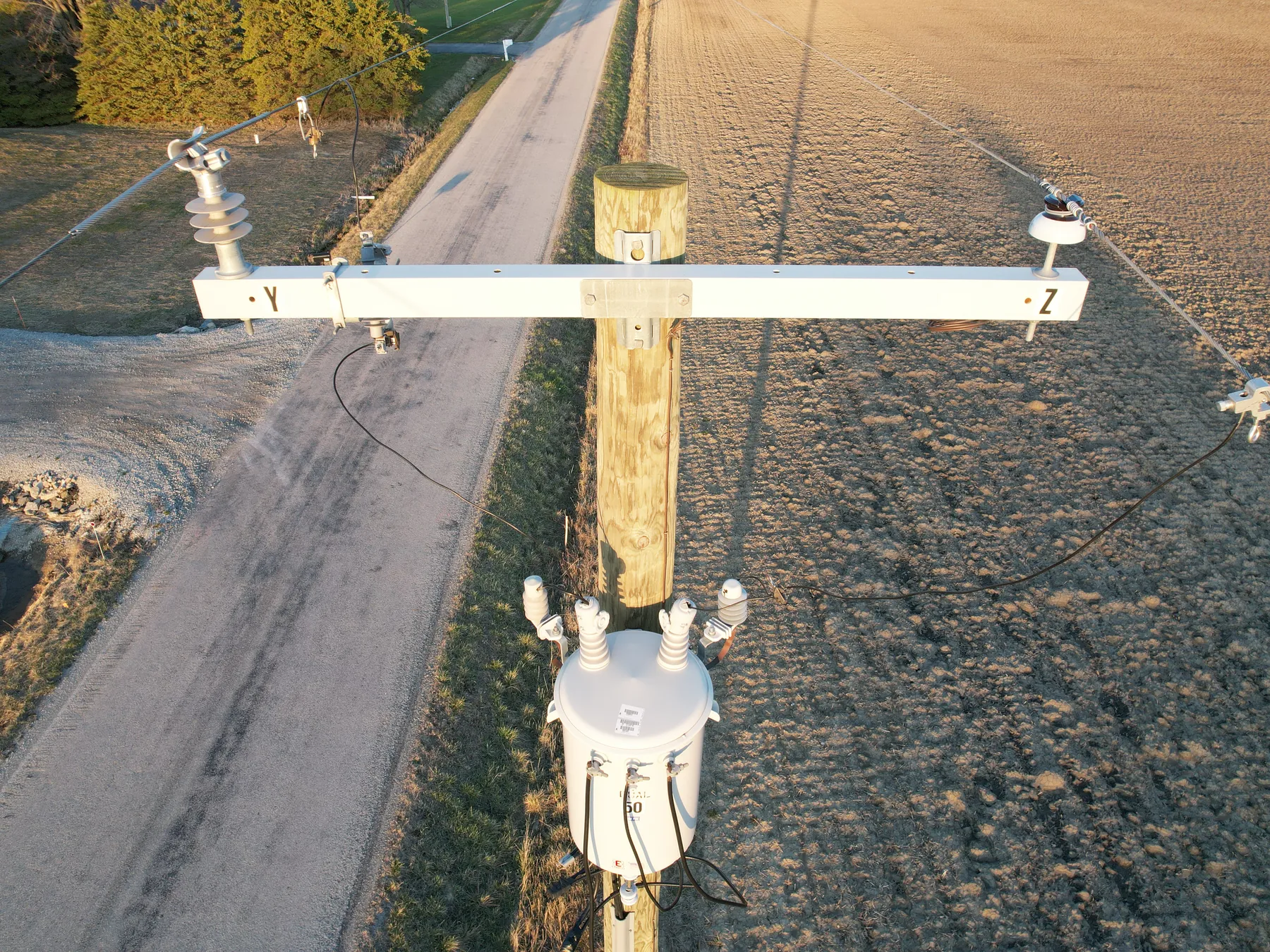 After: drone view of a new wooden pole with a new white crossarm and a new transformer beside the same rural road